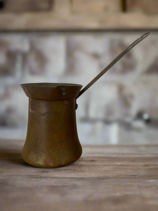 Vintage-style metal pot with handle on a wooden surface against a tiled wall.