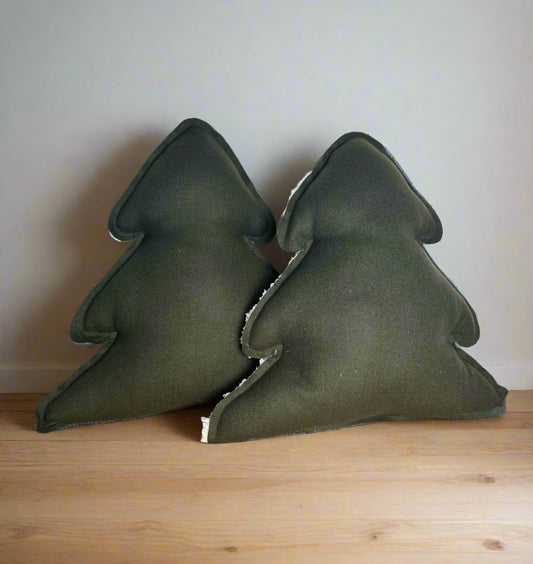 Two dark green tree-shaped cushions on a wooden surface with a light gray background