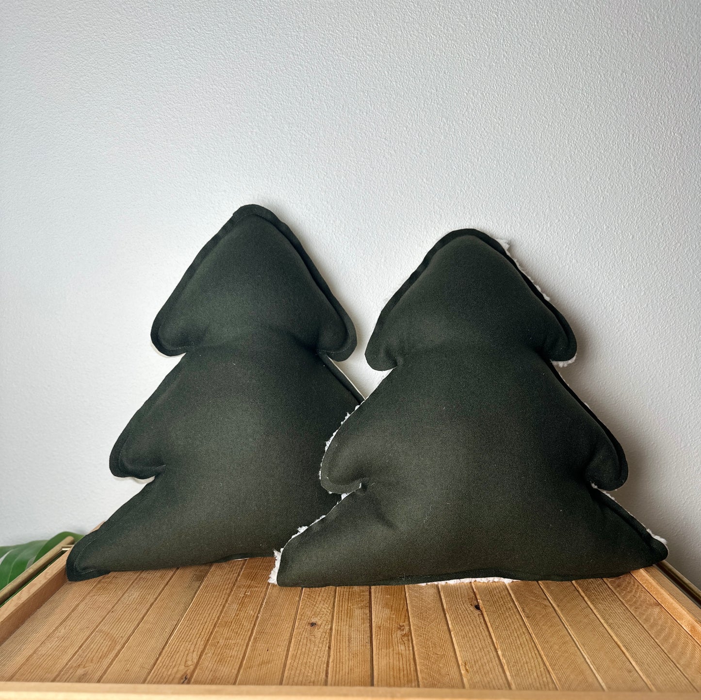 Two dark green triangular pillows on a wooden surface with a light gray wall background