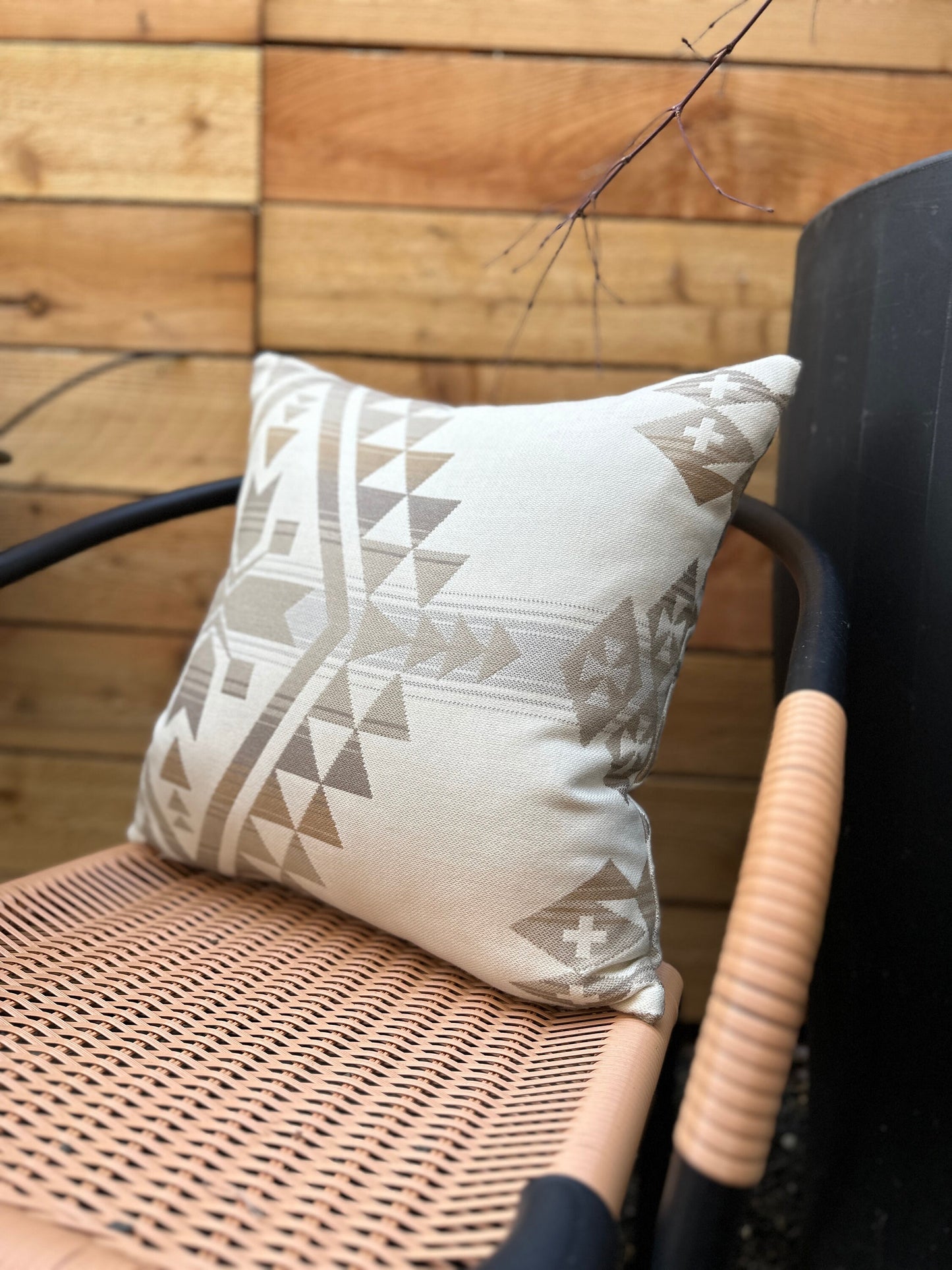 Decorative pillow with geometric pattern on a wicker chair against a wooden wall.