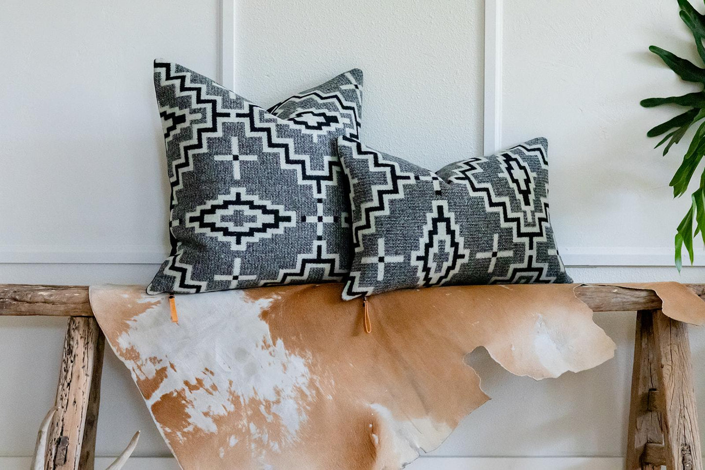 Two patterned pillows on a wooden bench with a cowhide rug underneath.