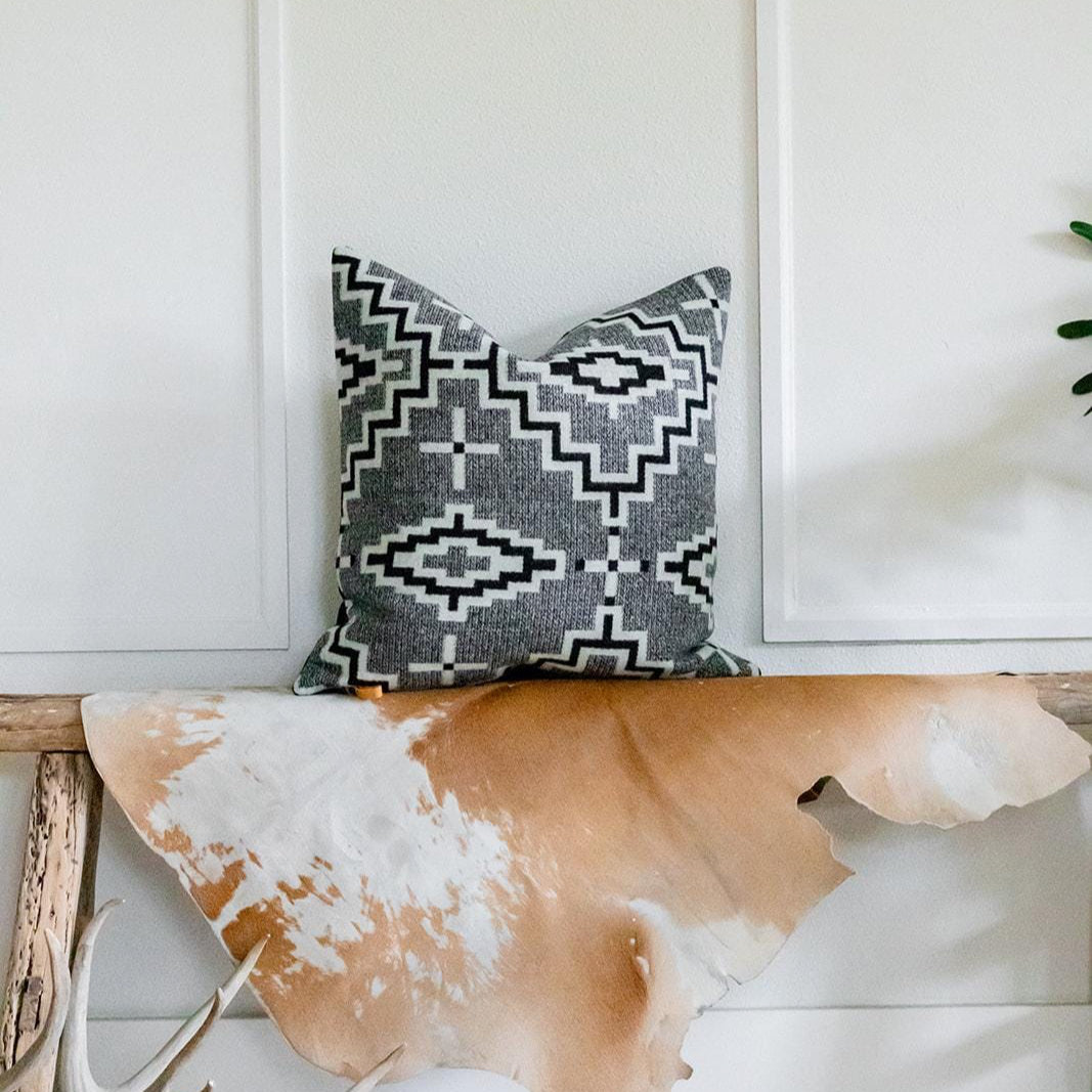 Decorative pillow with geometric pattern on a wooden bench against a white wall.