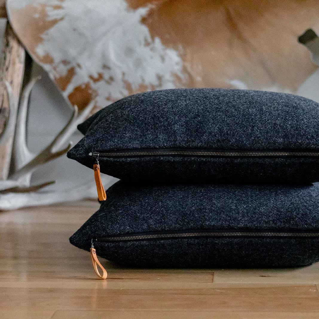 Two dark gray pillows with orange tassels on a wooden floor, with antlers in the background.