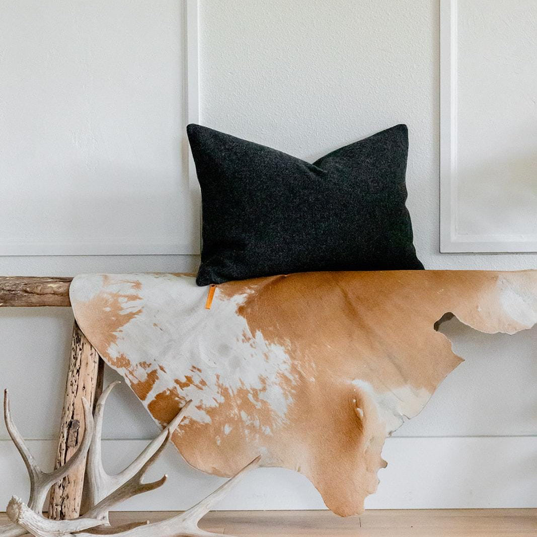 dark gray pillow on a wooden bench with a cowhide rug and deer antlers in a room