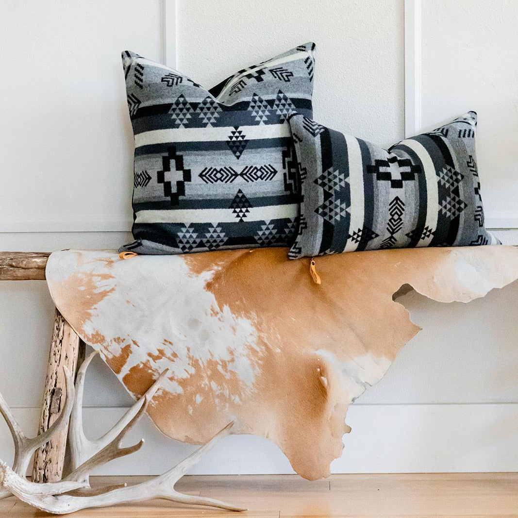 Decorative pillows with geometric patterns on a wooden bench against a white paneled wall.