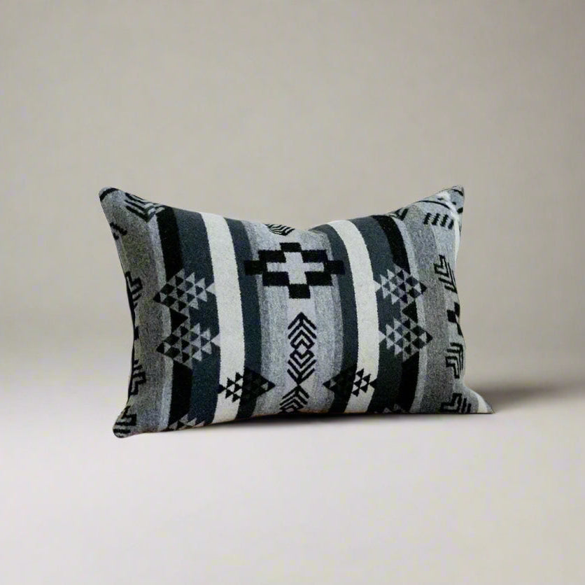 Decorative pillow with geometric pattern on a wooden bench against a white wall.
