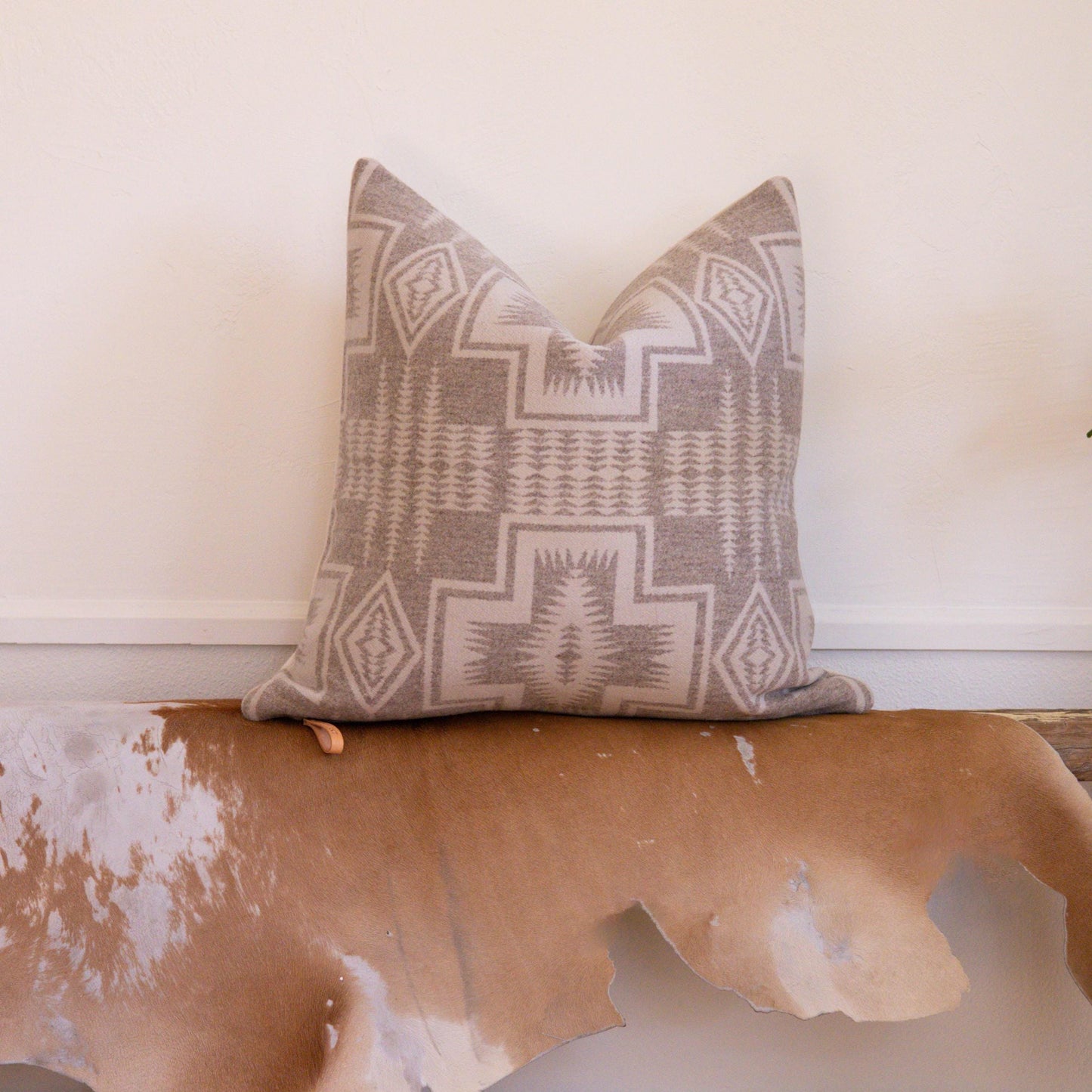 Decorative pillow with geometric pattern on a cowhide rug against a white wall.