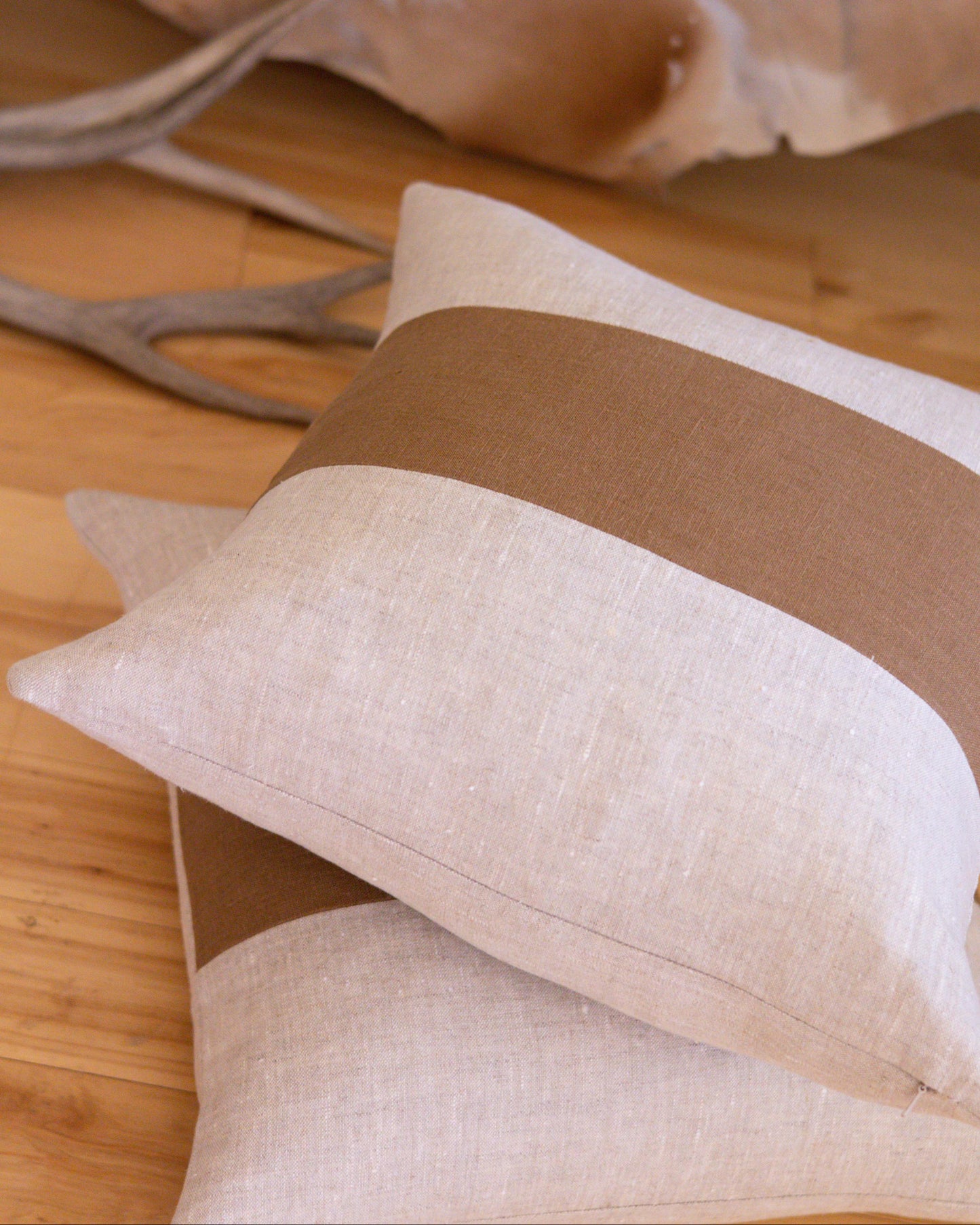 Beige and brown pillows on a wooden surface with antlers in the background