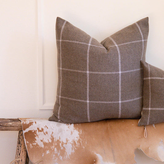 Plaid pillows on a wooden bench with a cowhide rug and antlers in the foreground.
