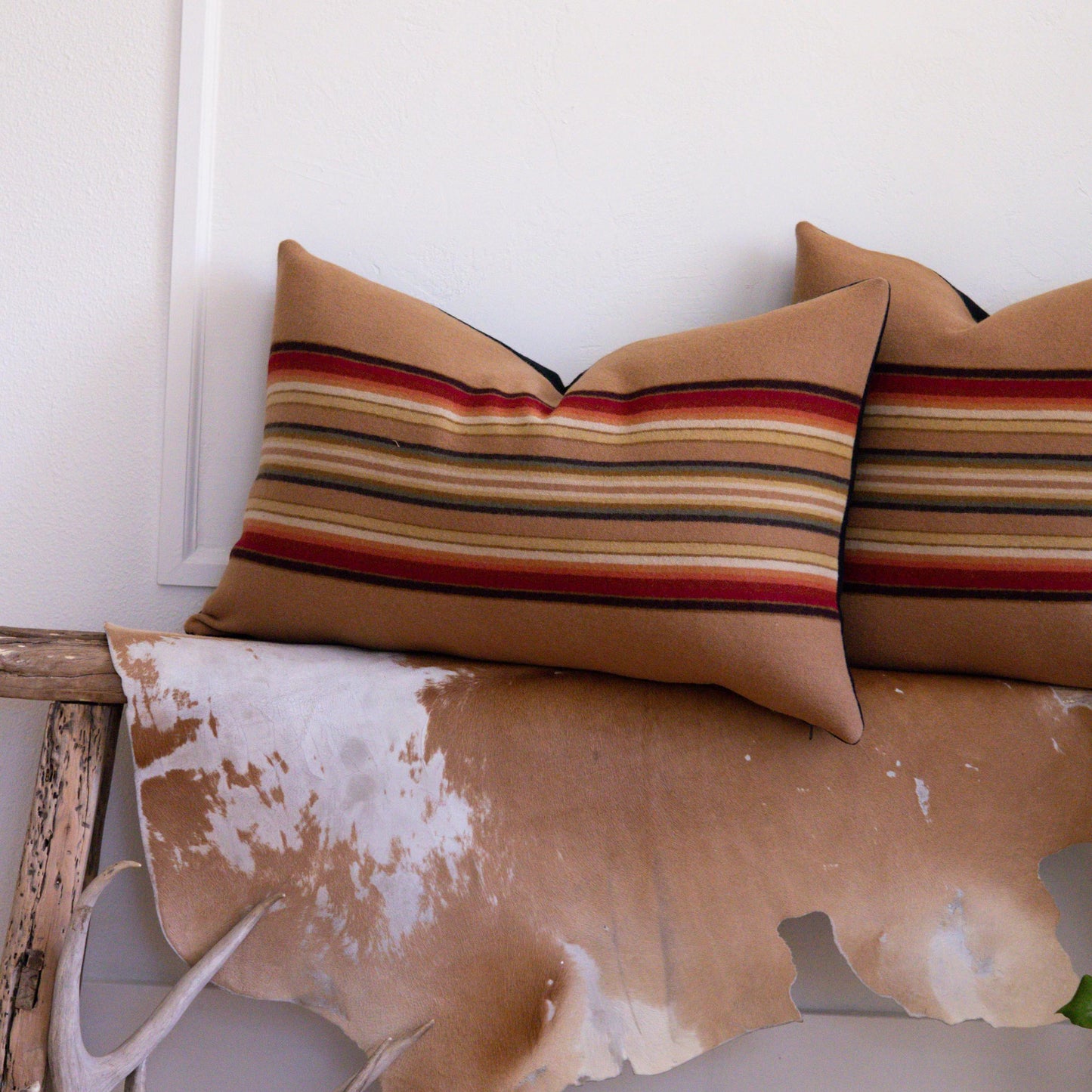 Decorative pillows with striped pattern and cowhide rug on a wooden surface.