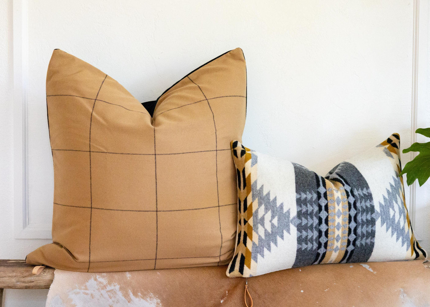 Two decorative pillows, one brown with a geometric pattern and the other with a tribal design, on a wooden surface.