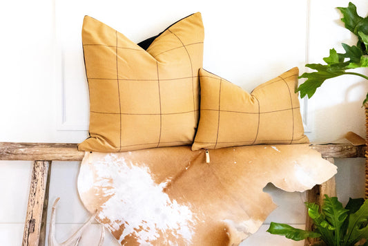 Two plaid-patterned pillows on a cowhide rug with a plant and wooden bench in the background.