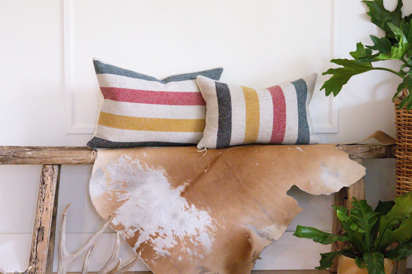 Decorative pillows with striped patterns on a wooden bench against a white wall.