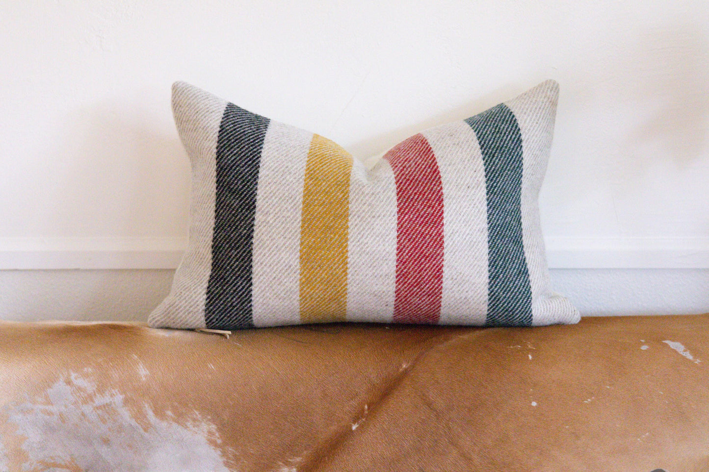 Striped pillow on a worn leather couch with a white wall background