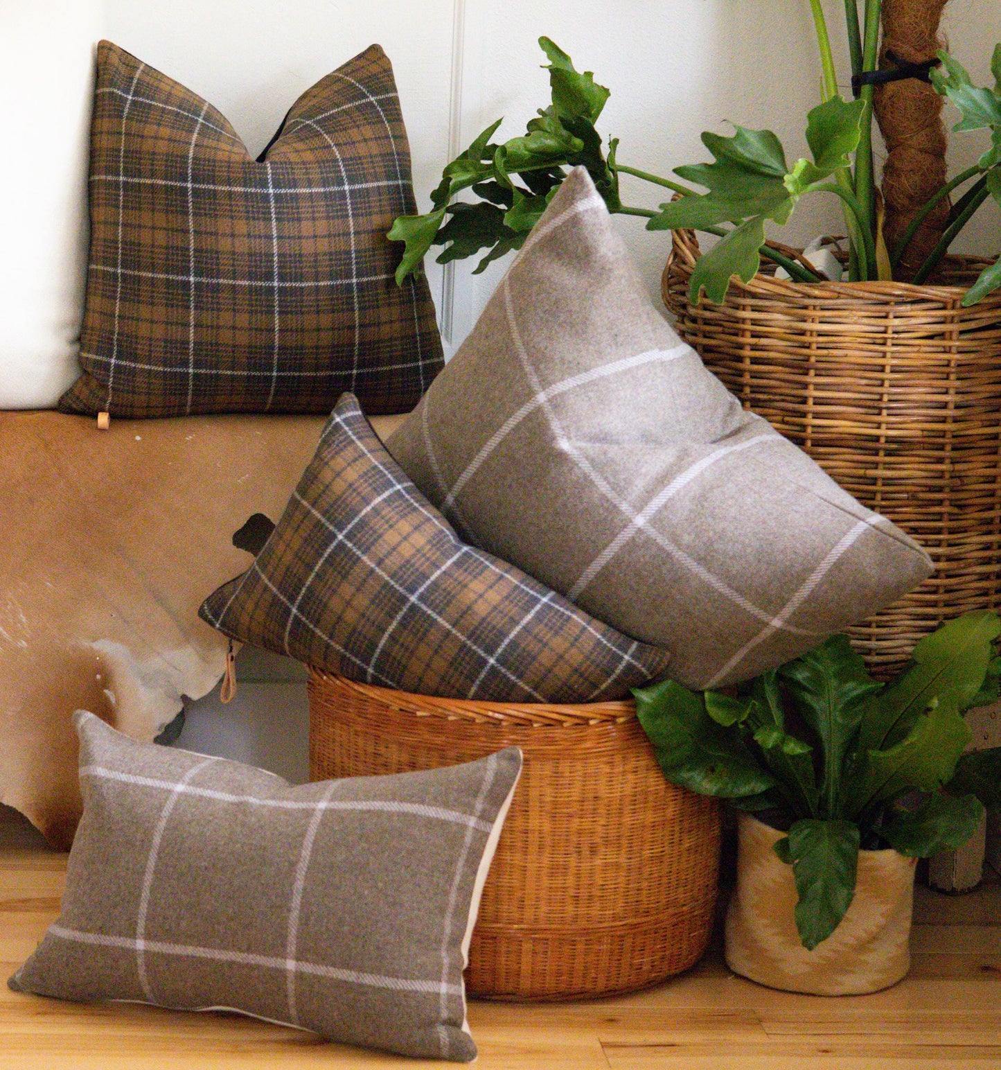 Plaid pillows in a wicker basket with plants on a wooden floor