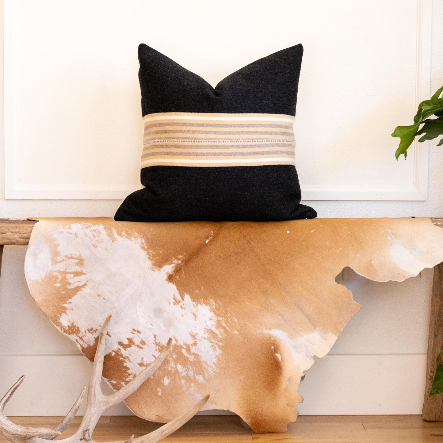 Decorative pillow on a wooden bench with cowhide rug and plants