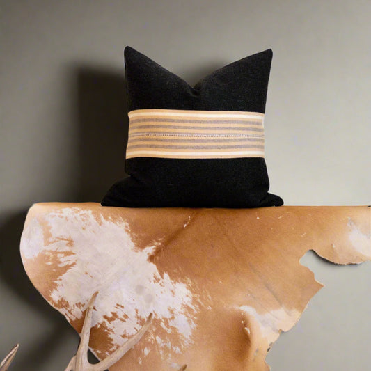 Black pillow with a beige band on a wooden bench with cowhide design, antlers in front.