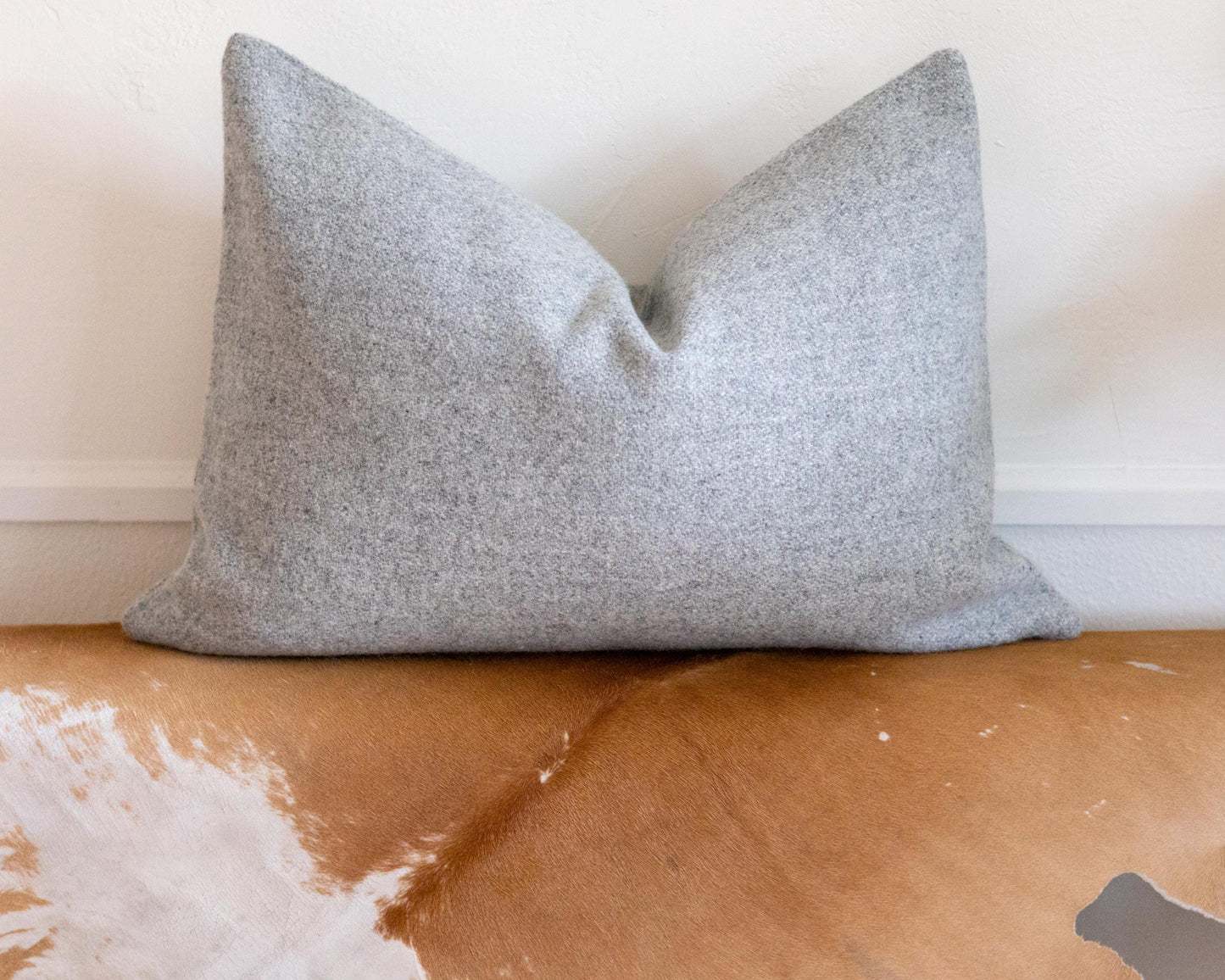 Gray pillow on a brown leather couch with a white wall background