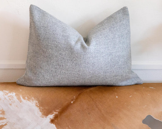 Gray pillow on a brown leather couch with a white wall background