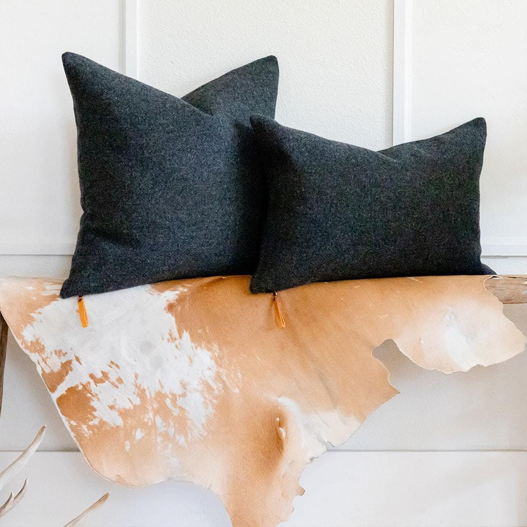 Two dark gray pillows on a wooden bench with a cowhide rug underneath.