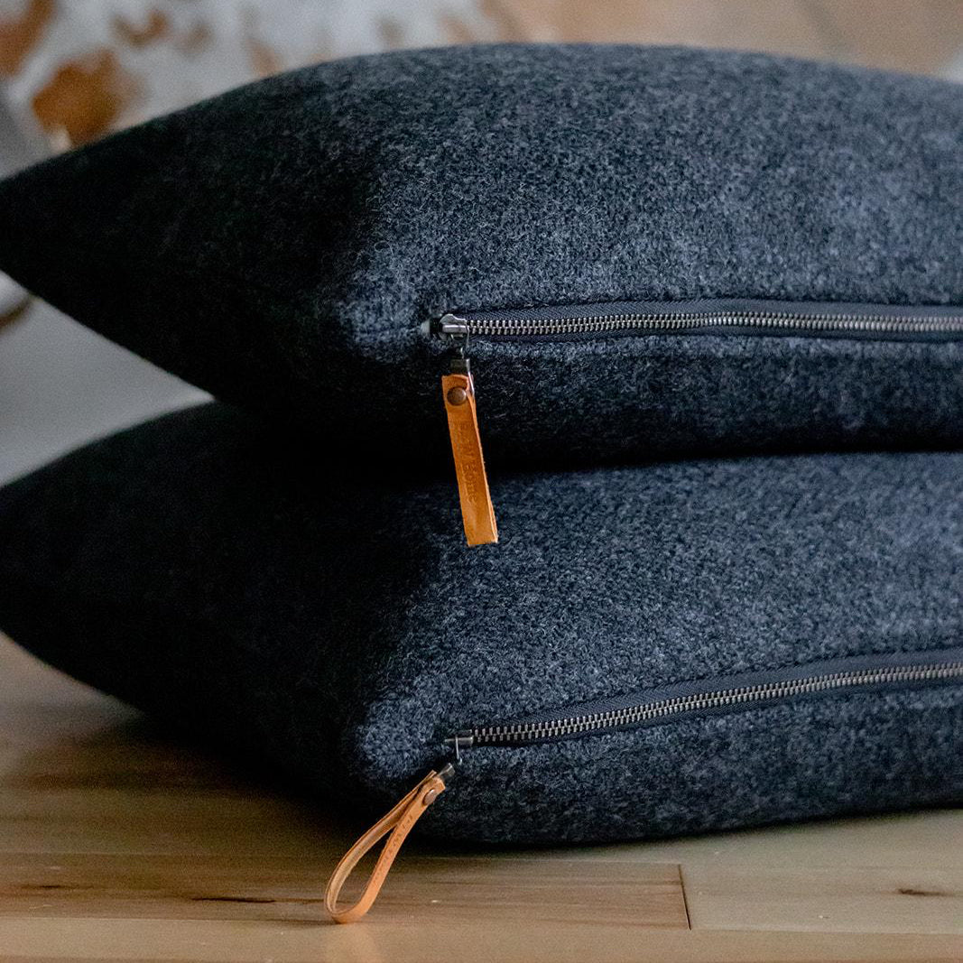 Two dark gray pillows with zipper details on a wooden surface.