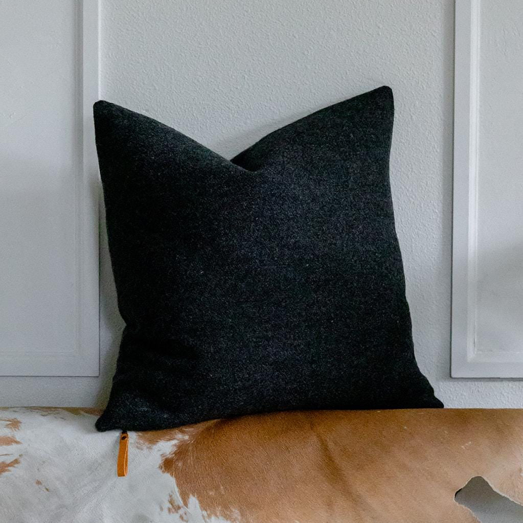 Charcoal gray pillow on a cowhide rug with a neutral wall background