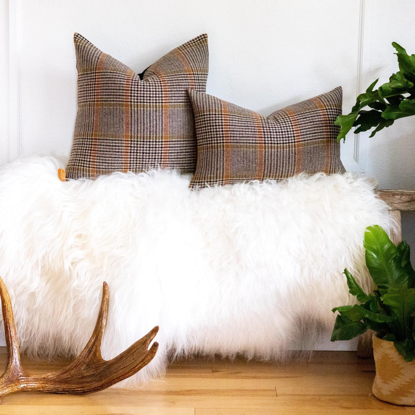 Fur-covered bench with plaid pillows and a plant in a room.