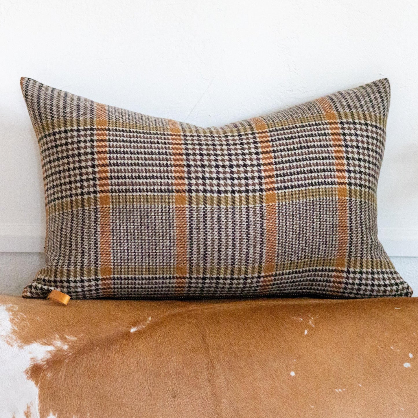 Plaid pillow on a worn leather couch with a white wall background