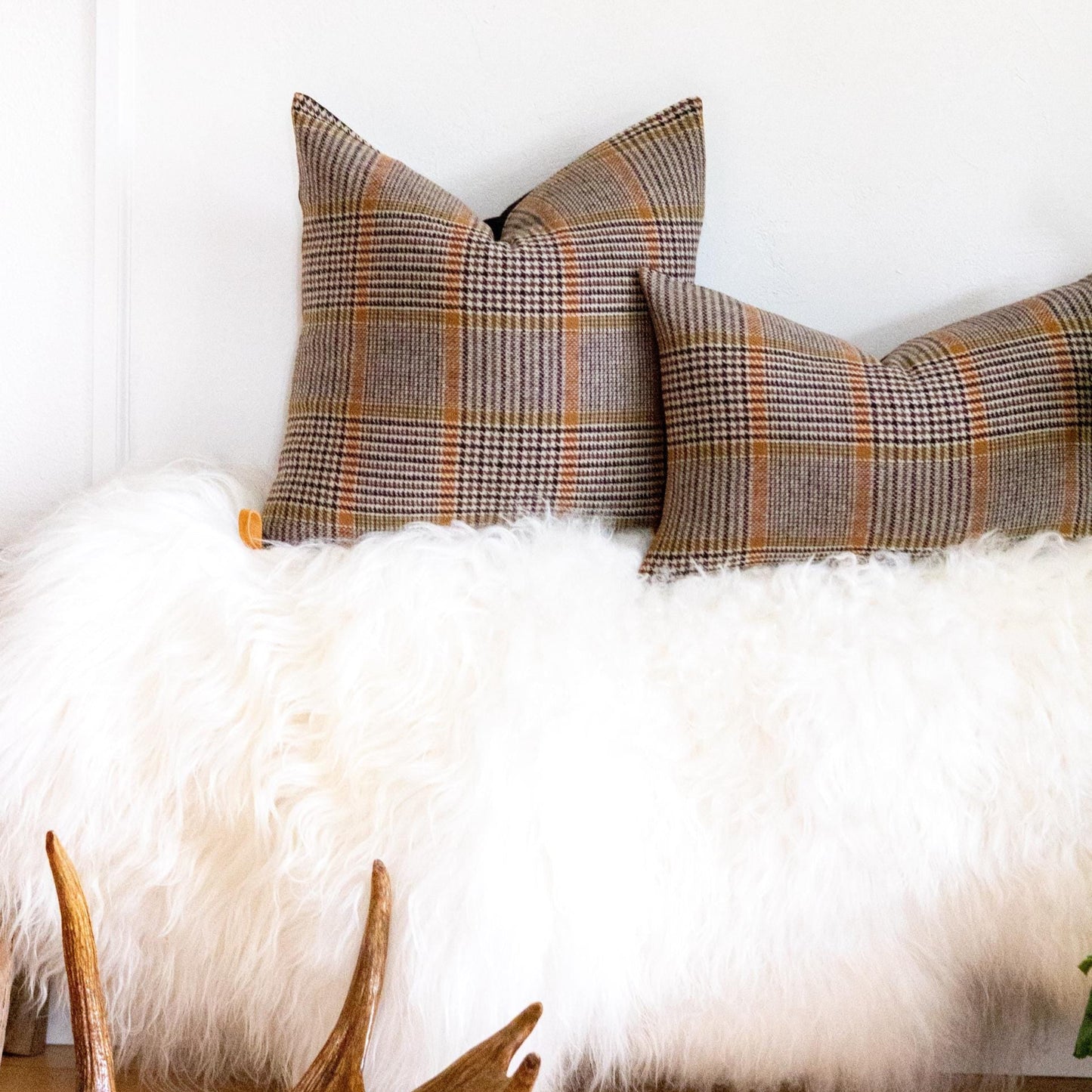Plaid pillows on a white fur surface with wooden antlers in the foreground.