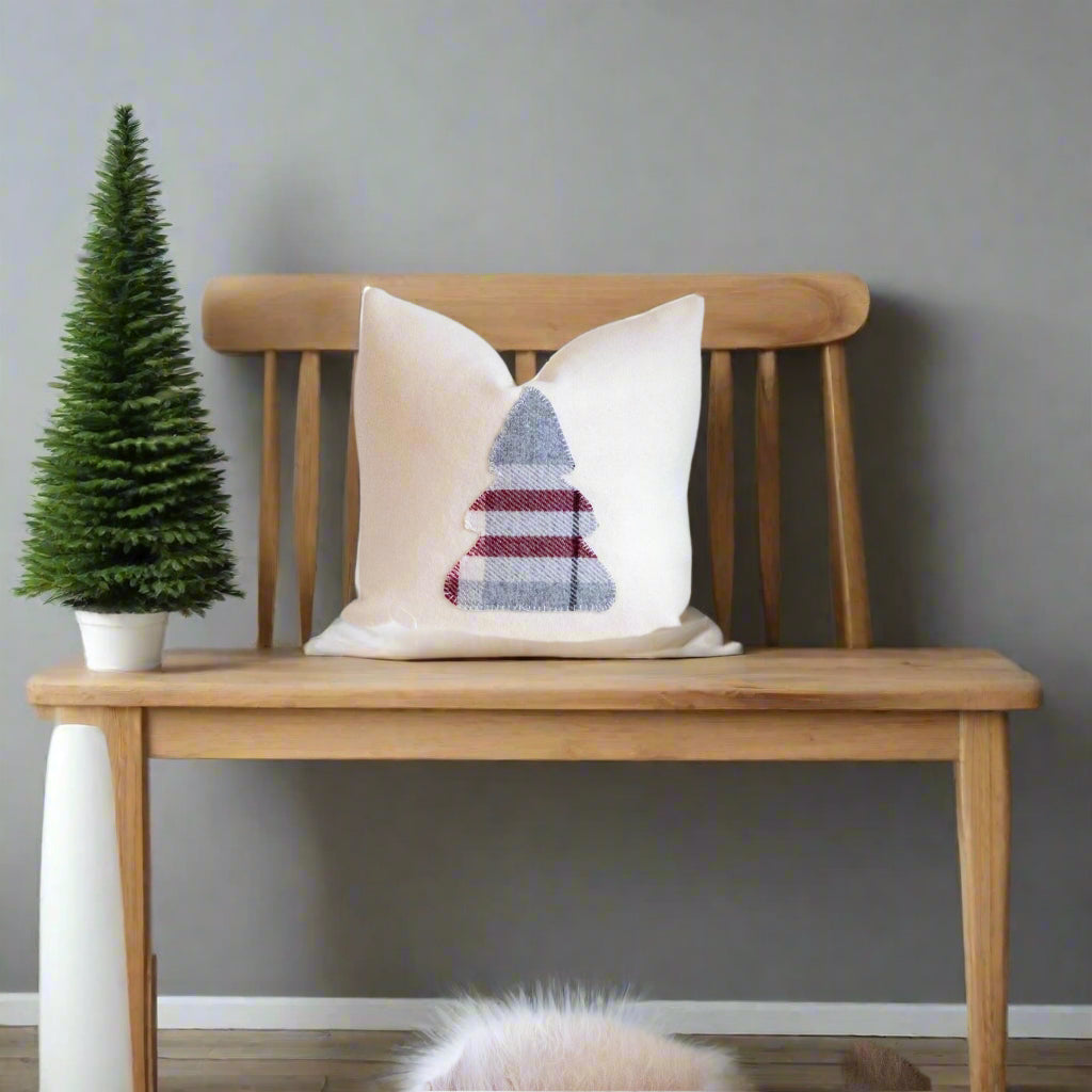 White pillow with a geometric pattern on a fluffy white chair next to a Christmas tree.