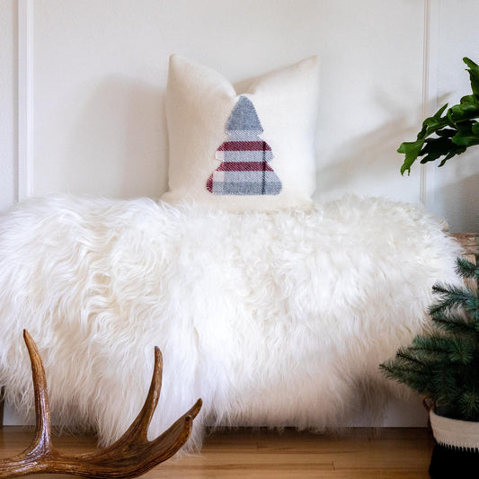 White fluffy chair with a decorative pillow featuring a Christmas tree design, surrounded by festive decor.