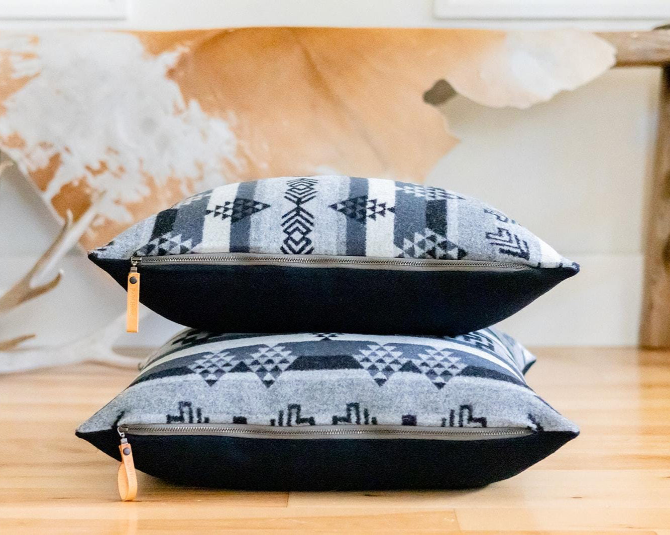 Two patterned pillows stacked on a wooden surface with a decorative cowhide rug in the background.