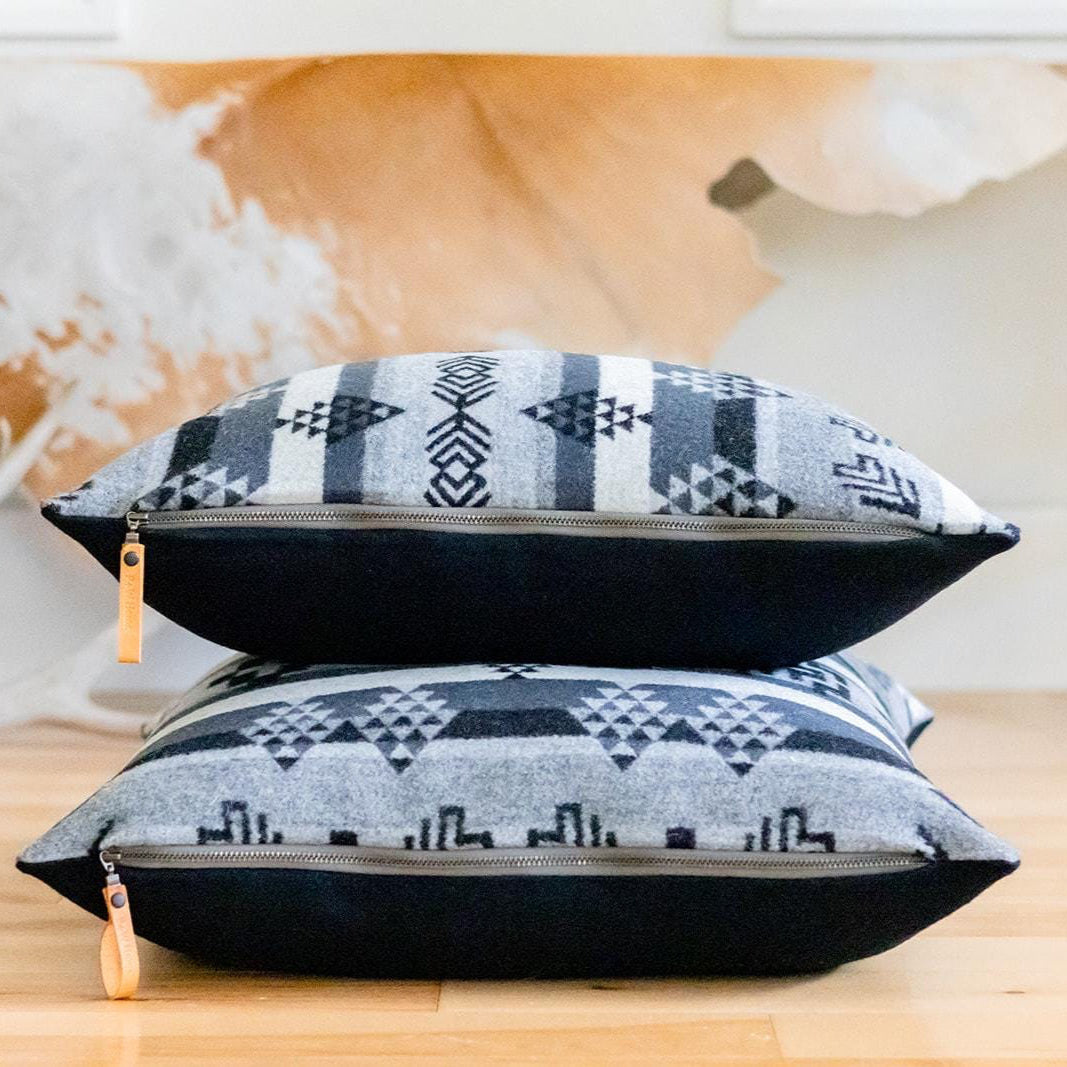 Two patterned pillows stacked on a wooden surface with a decorative cowhide rug in the background.