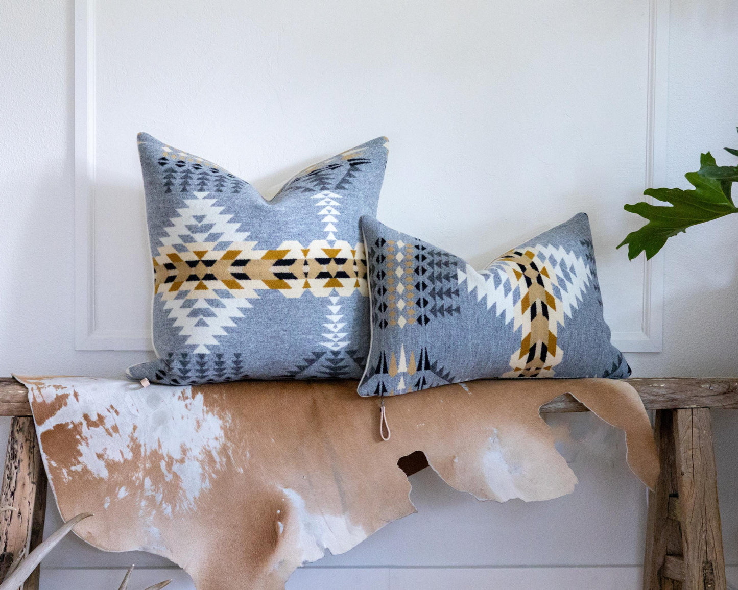 Two patterned pillows on a wooden bench with a cowhide rug against a white wall.