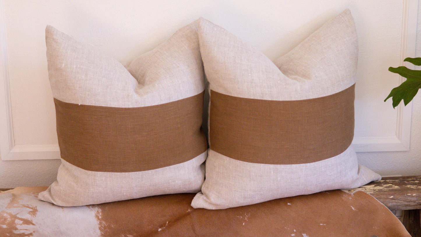 Two beige pillows with brown bands on a wooden surface.