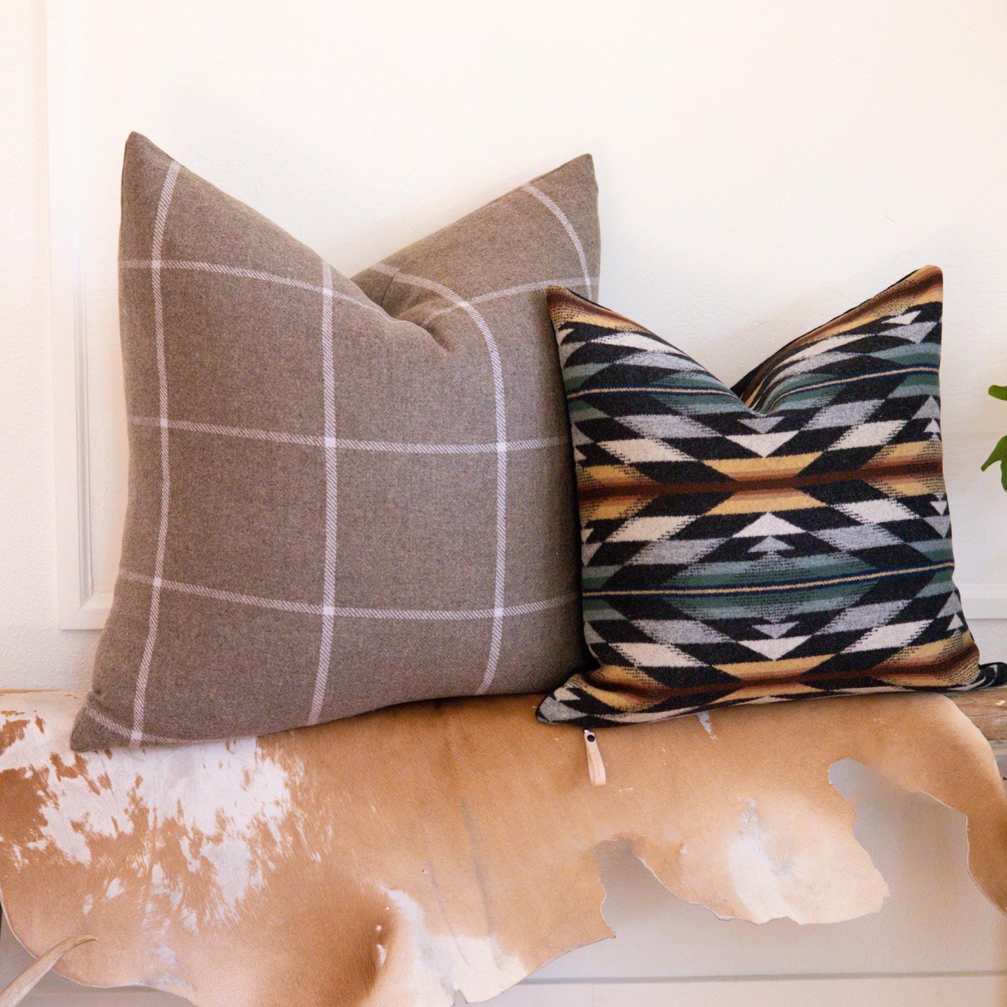 Two decorative pillows on a cowhide rug with a white wall background