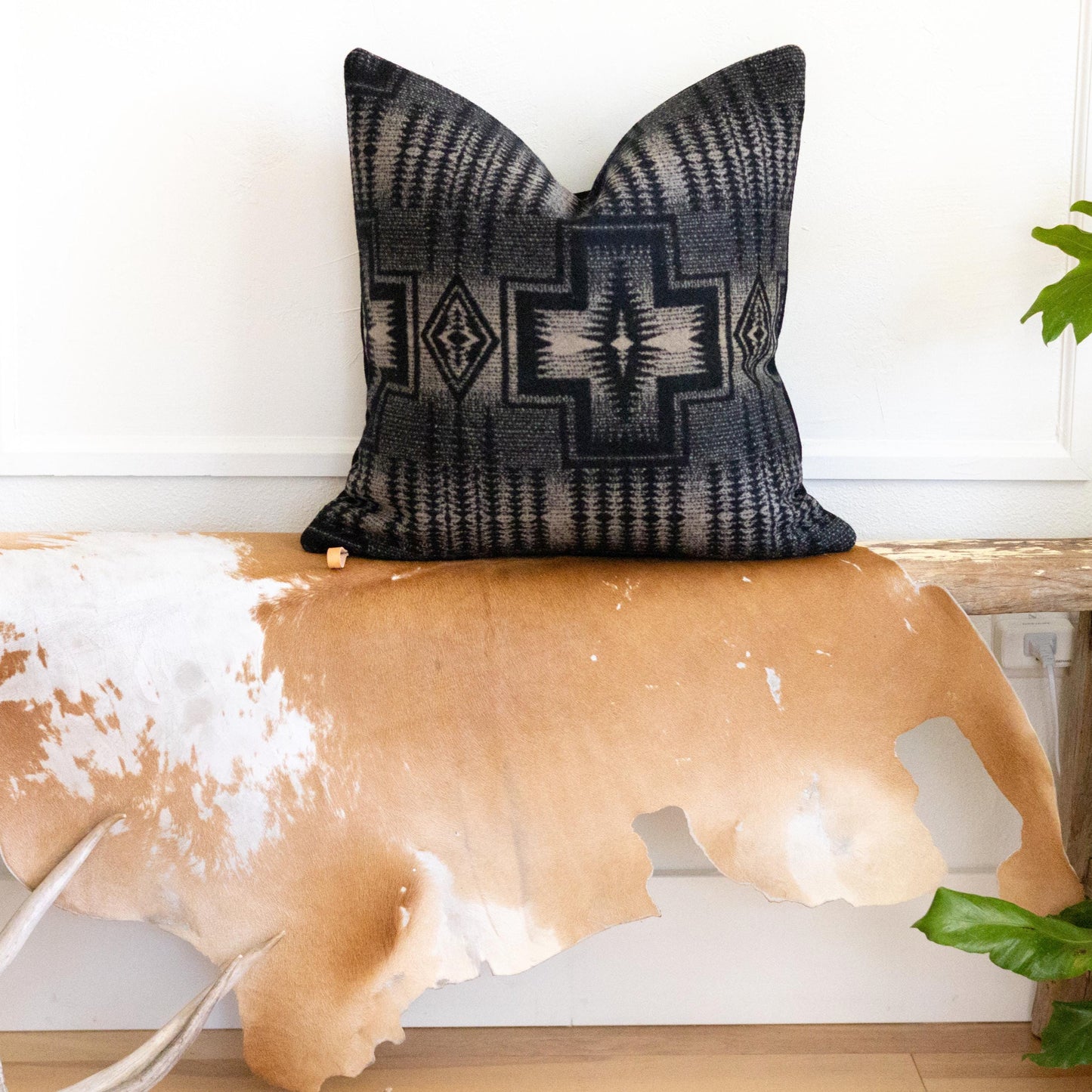 Decorative pillow with geometric black and tan pattern on a cowhide bench