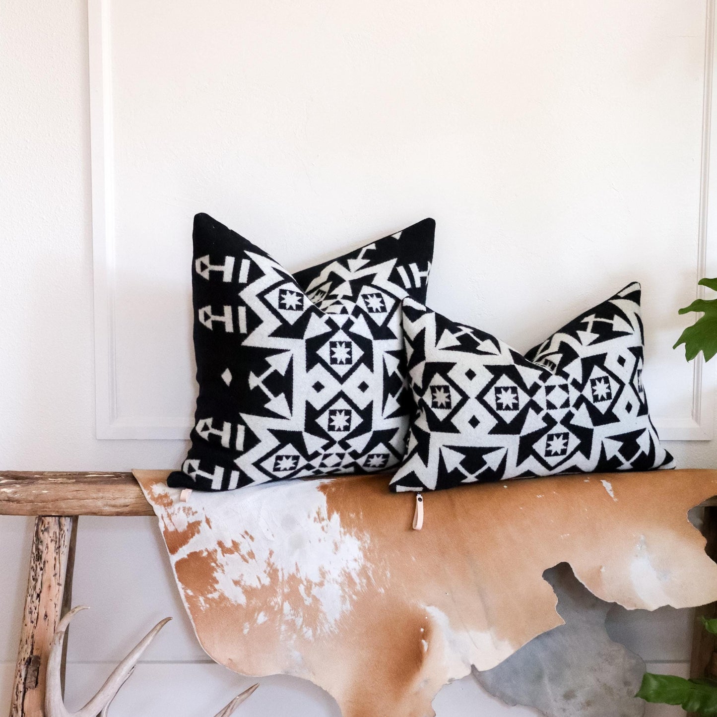 Two black and white patterned pillows on a wooden bench with a white wall background.