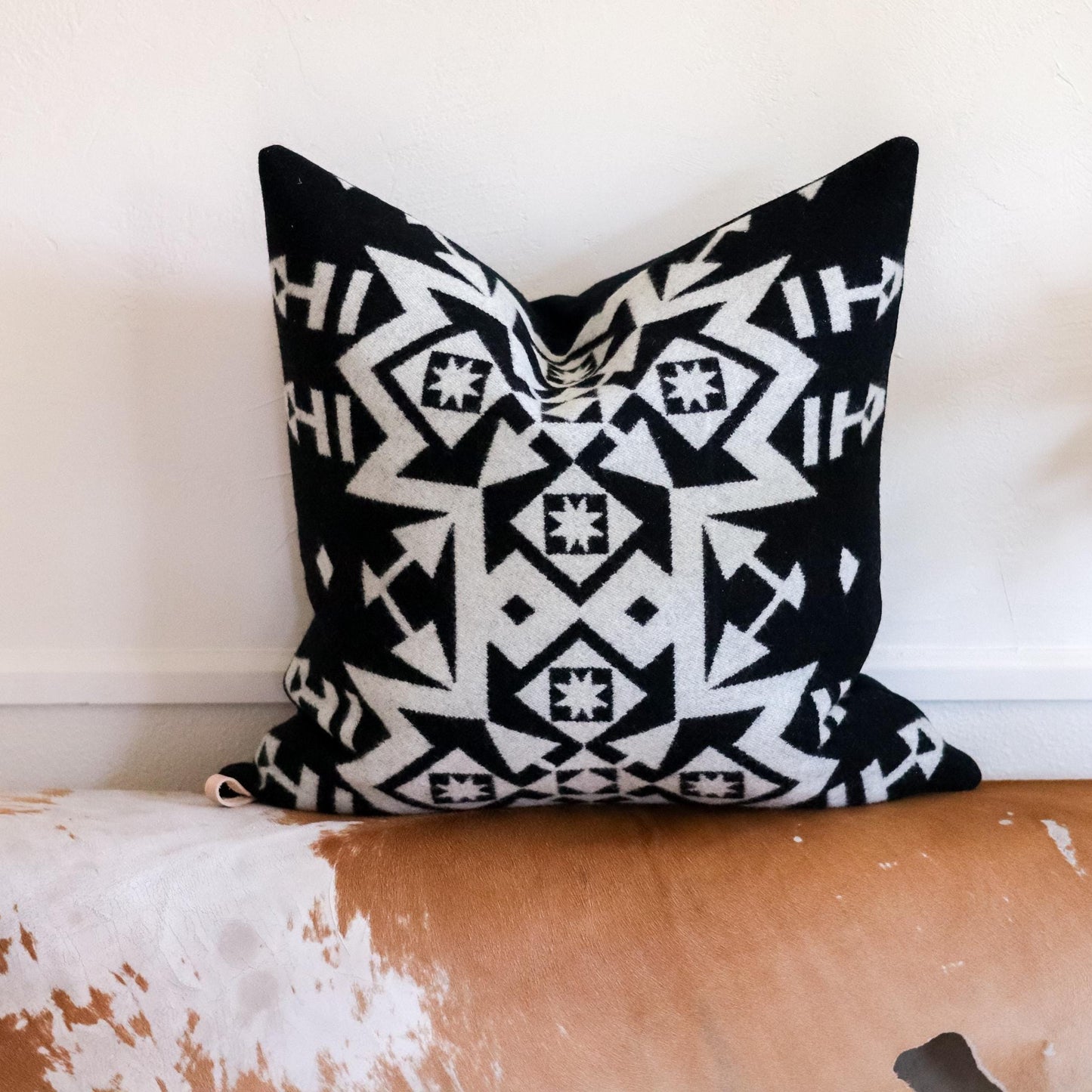 Black and white patterned pillow on a wooden bench with a white wall background