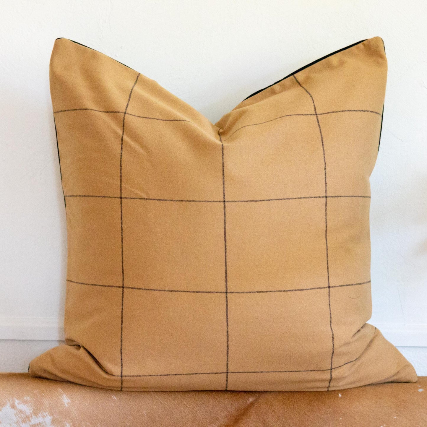 Beige pillow with black grid pattern on a wooden surface