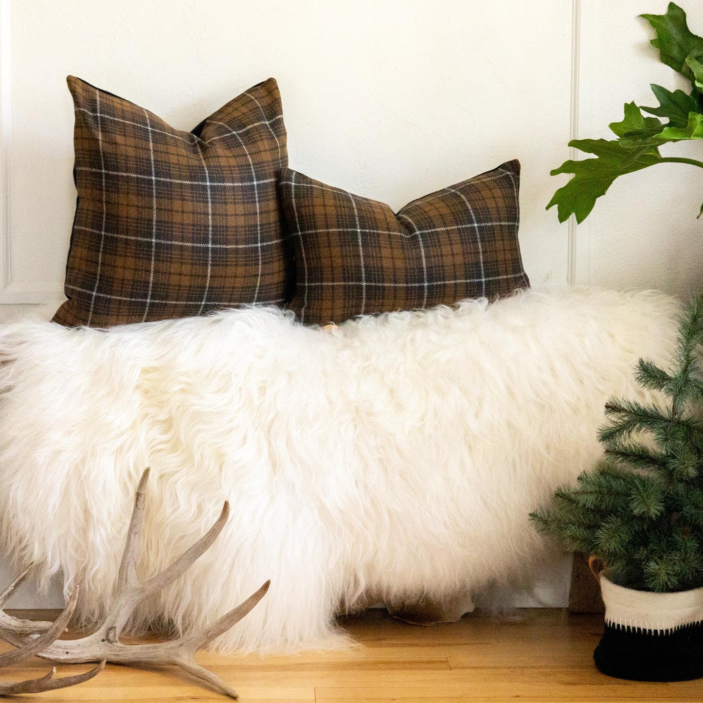 Decorative bench with plaid pillows, white fur throw, and a plant in a room.