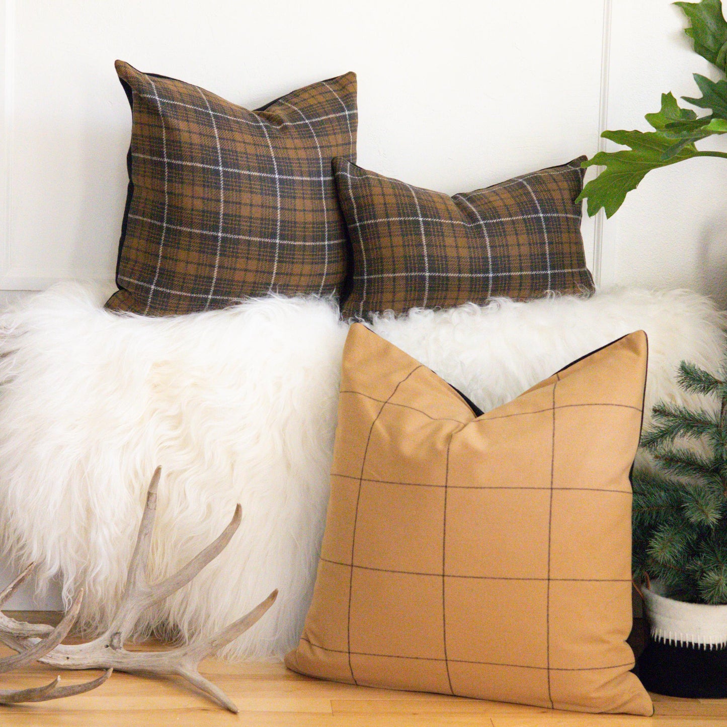 Plaid and checkered pillows on a white surface with a plant and wooden bench in the background.