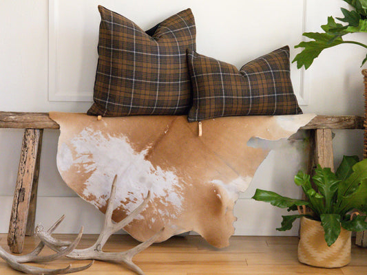 Plaid pillows on a cowhide rug with a wooden bench and plant in the background