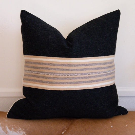Black pillow with striped pattern on a beige surface