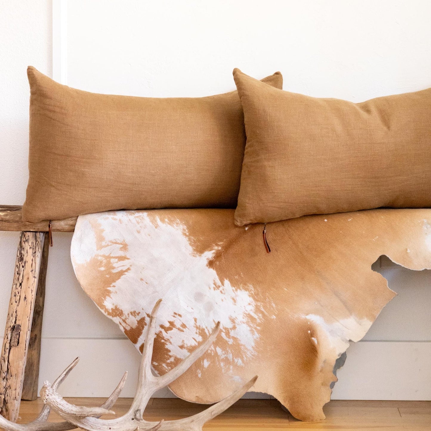 Two brown pillows on a wooden bench with a cowhide rug underneath.