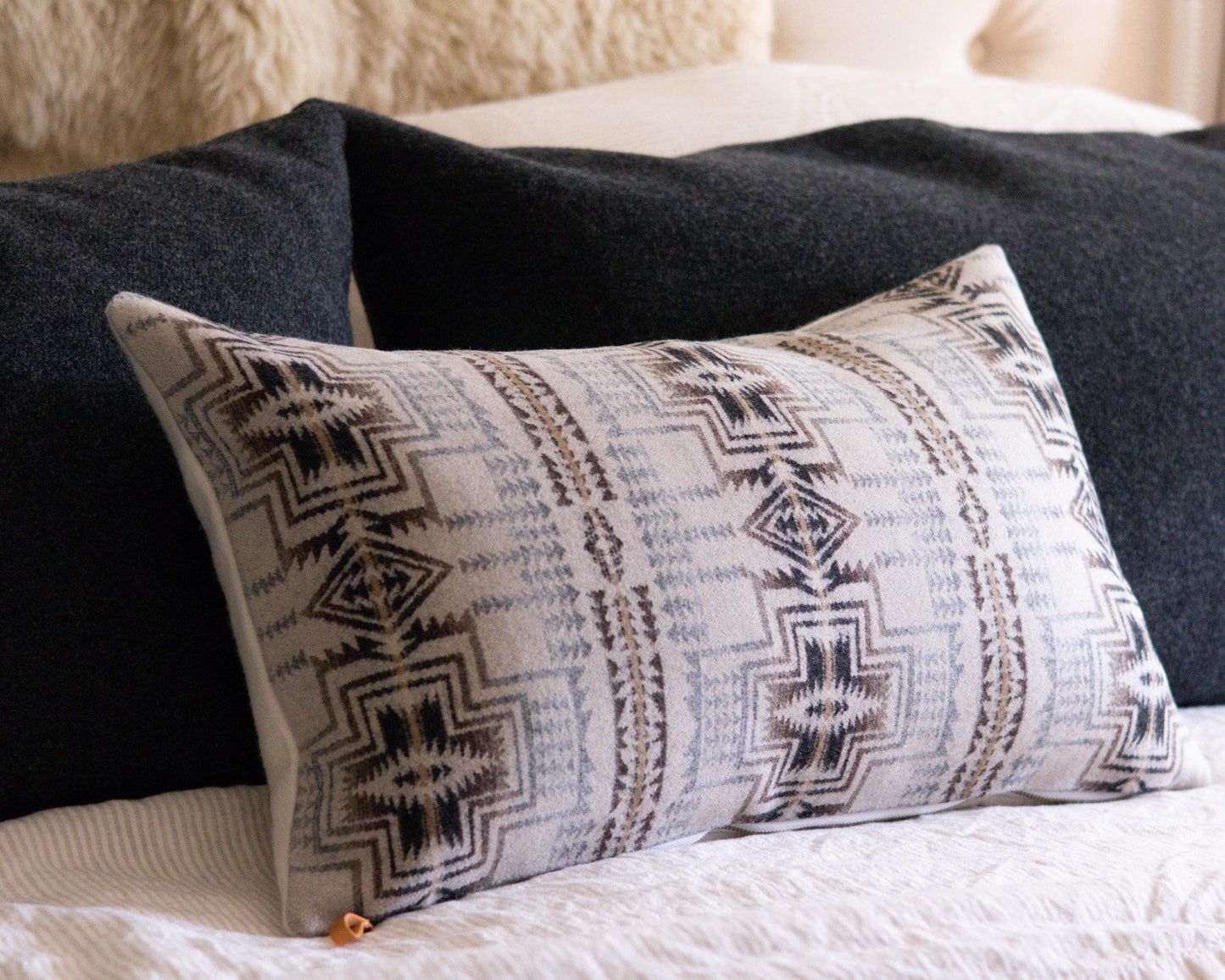 Decorative Pendleton® pillow with tribal pattern on a bed with dark pillows