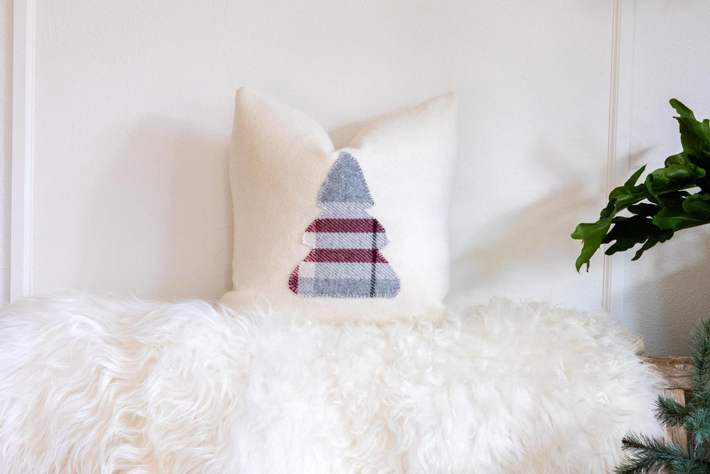 Decorative pillow with a tree pattern on a fluffy white chair against a white wall.