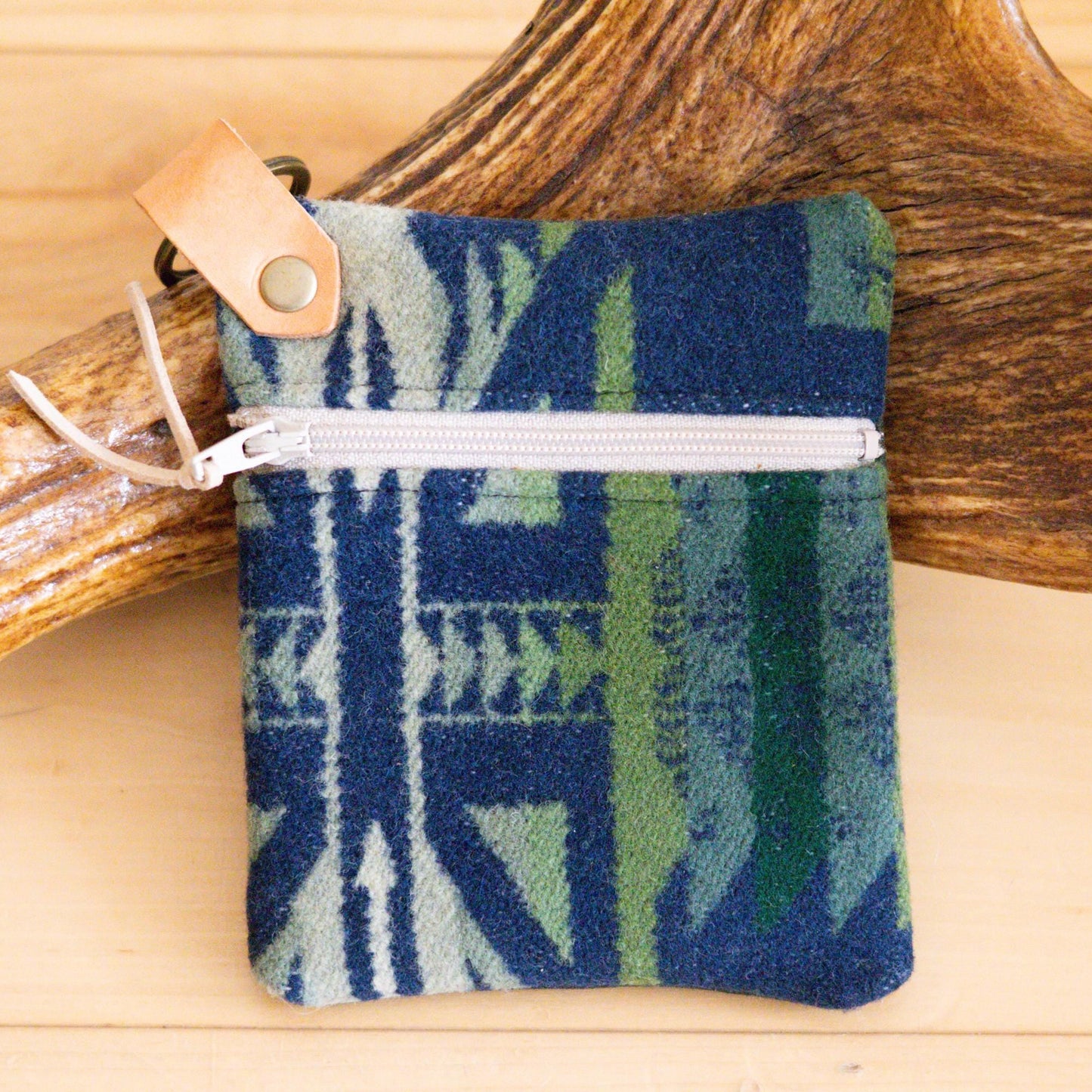 Blue and green patterned pouch with a white zipper on a wooden surface