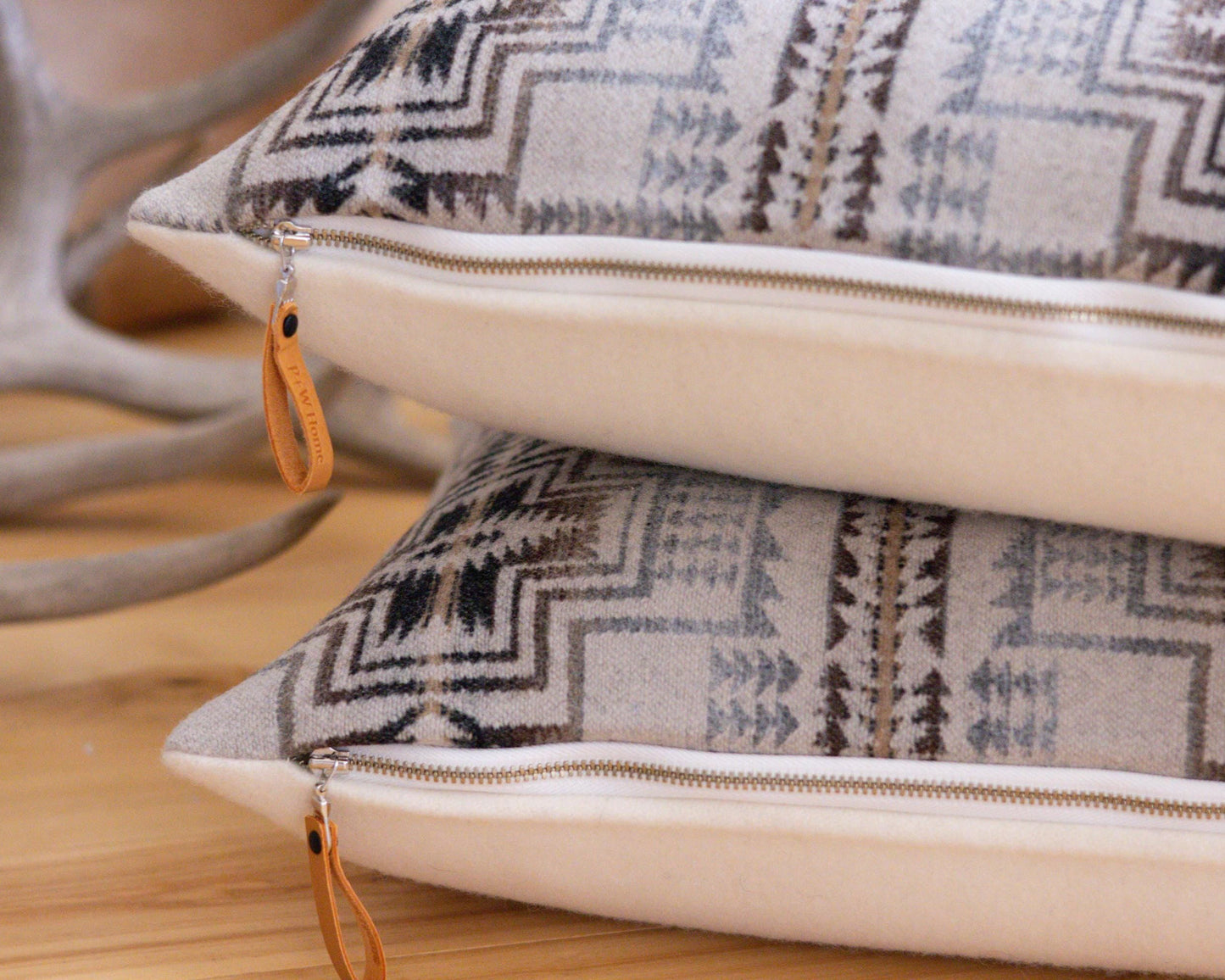 Two patterned Pendleton® pillows with branded zippers on a wooden surface