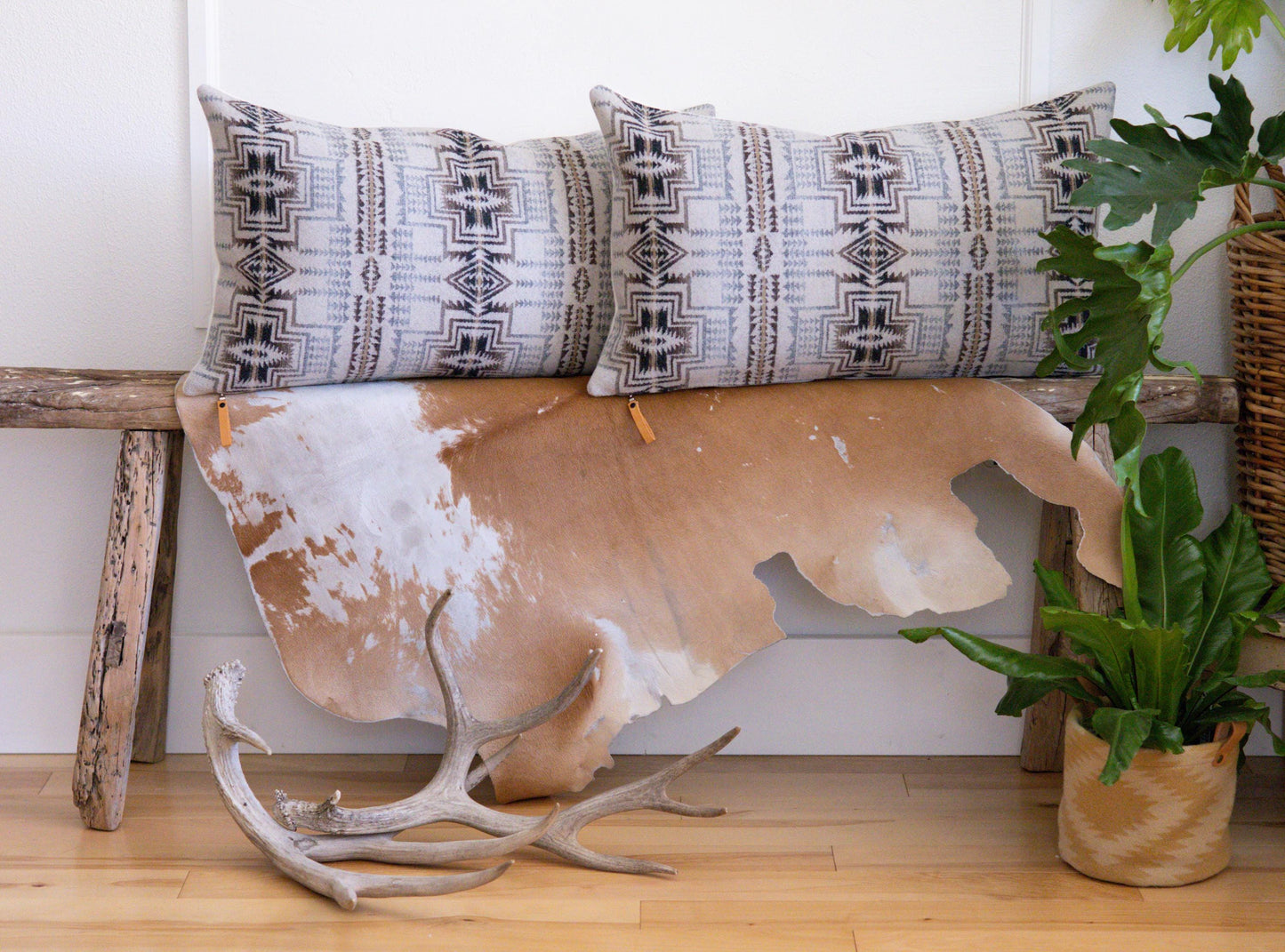 Decorative pillows with geometric patterns on a cowhide rug with antlers, against a white wall.